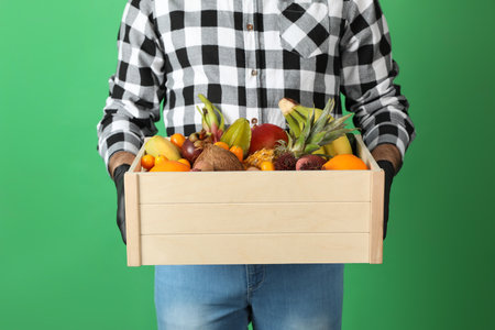 Courier holding crate with assortment of exotic fruits on green background, closeupの写真素材