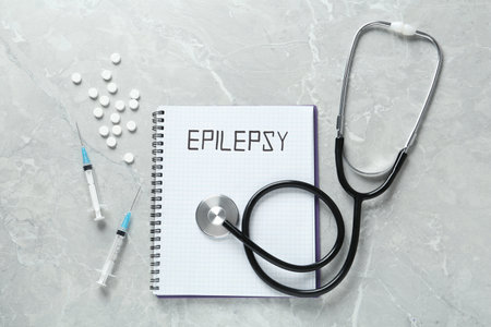 Notebook with word Epilepsy, stethoscope, pills and syringes on gray marble table, flat layの写真素材
