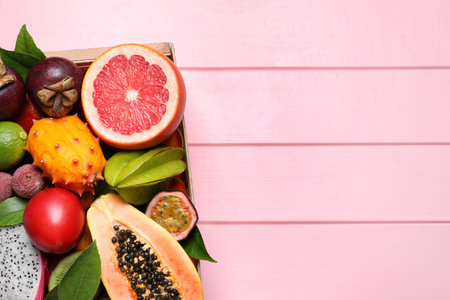 Different tropical fruits in box on pink wooden background, top view. Space for textの写真素材