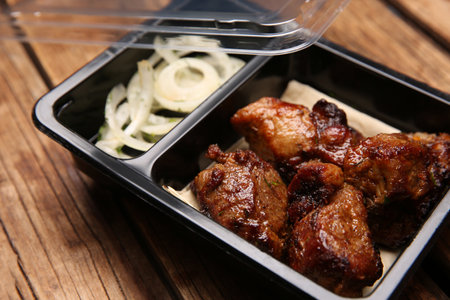 Plastic container of tasty shish kebab on wooden table, closeup. food delivery serviceの写真素材