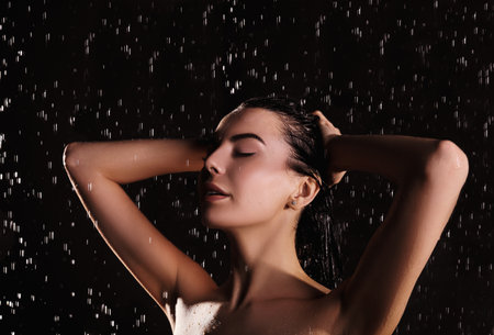 Young woman washing hair while taking shower on black backgroundの写真素材