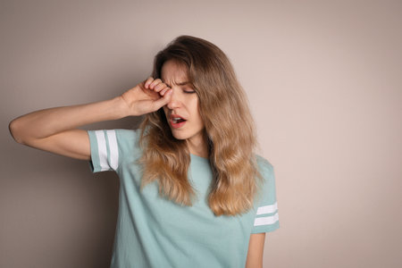 Young tired woman yawning on beige backgroundの写真素材