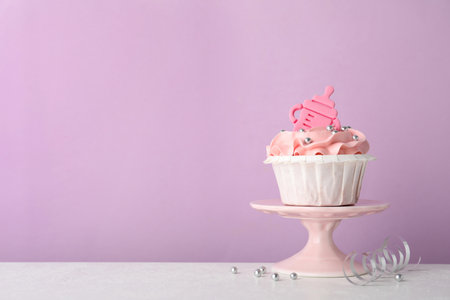 Baby shower cupcake with pink cream and topper on white table against violet background, space for textの写真素材