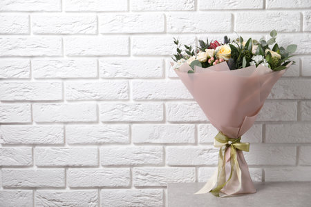 Beautiful bouquet with roses on light table near white brick wall. Space for textの写真素材