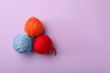 Soft colorful woolen yarns on lilac background, flat lay. Space for textの写真素材