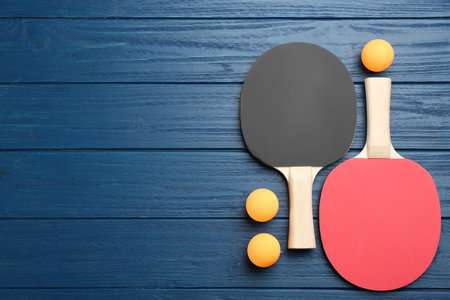 Table tennis rackets and balls on blue wooden table, flat lay. Space for textの写真素材