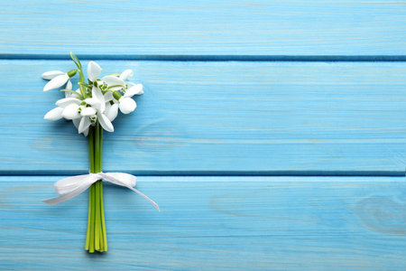 Beautiful bouquet of snowdrops on light blue wooden table, top view. Space for textの写真素材