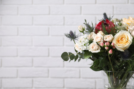 Beautiful bouquet with roses against white brick wall, closeup. Space for textの写真素材