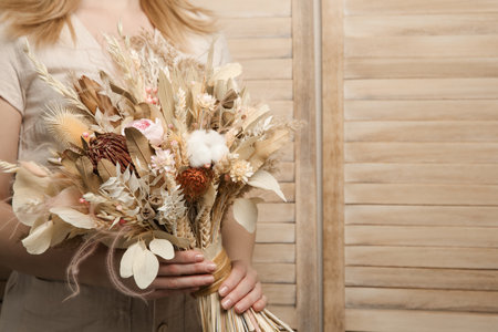 Woman holding beautiful dried flower bouquet on wooden background, closeup. Space for textの写真素材