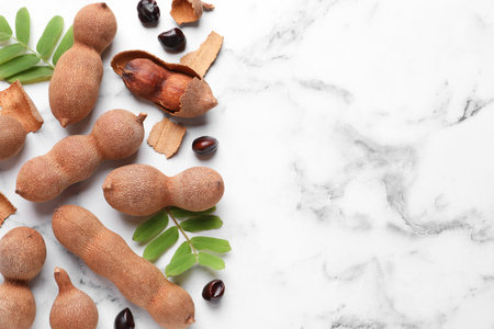 Ripe tamarinds and fresh leaves on white marble table, flat lay. Space for textの写真素材