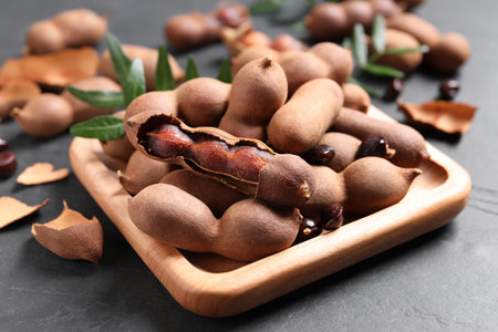 Wooden plate with delicious ripe tamarinds on black tableの写真素材