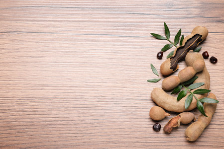 Delicious ripe tamarinds and leaves on wooden table, flat lay. Space for text