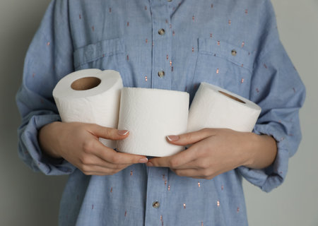 Woman with heap of toilet paper rolls on gray background, closeupの写真素材