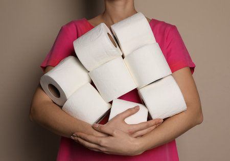 Woman with heap of toilet paper rolls on beige background, closeupの写真素材