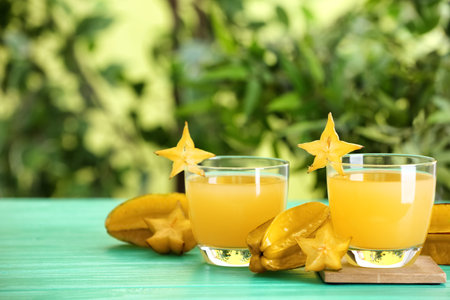 Delicious carambola juice and fresh fruits on light blue wooden table against blurred background. Space for textの写真素材