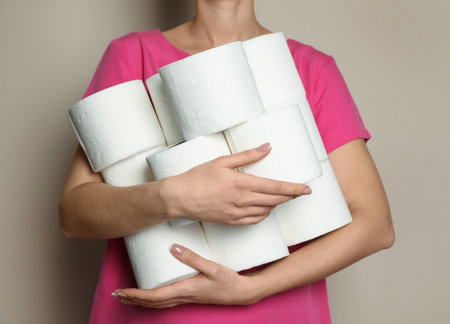 Woman with heap of toilet paper rolls on beige background, closeupの写真素材