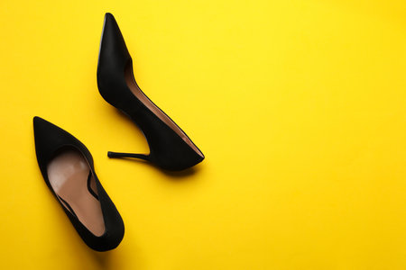 Pair of elegant black high heel shoes on yellow background, flat lay. Space for textの写真素材