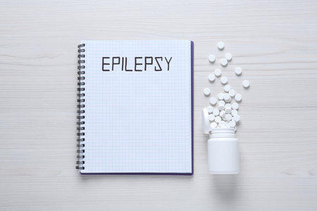 Notebook with word Epilepsy and pills on white wooden table, flat layの写真素材