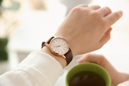 Woman with luxury wristwatch and cup of tea on blurred background, closeupの写真素材