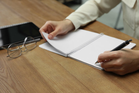 Left-handed woman writing in notebook at wooden table, closeupの写真素材