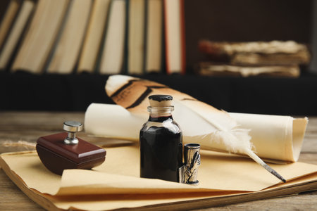 Feather pen, bottle of ink, notebook and parchment scroll on wooden tableの写真素材