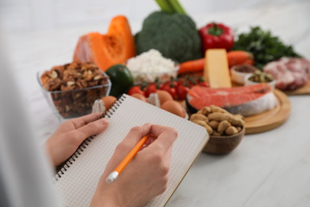 Woman with notebook and healthy food at white table, closeup. Keto dietの写真素材
