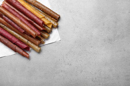 Delicious fruit leather rolls on gray table, flat lay. Space for textの写真素材