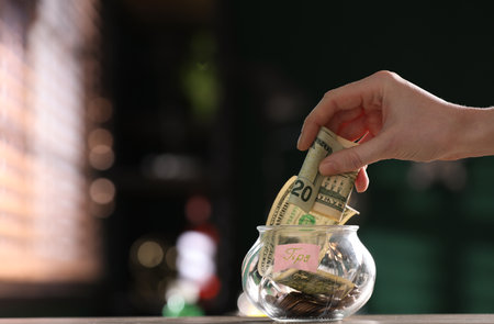 Woman tips into glass vase on wooden putting table indoors, closeup. Space for textの写真素材