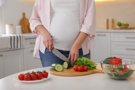 Young pregnant woman preparing vegetable salad at table in kitchen, closeup. healthy eatingの写真素材
