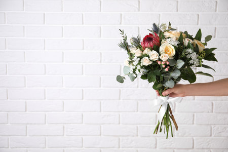 Woman with bouquet of beautiful roses near white brick wall, closeup. Space for textの写真素材