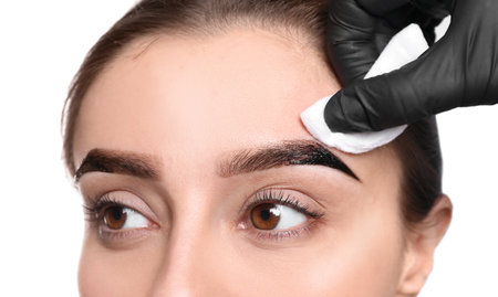 Beautician wiping tint from woman's eyebrows on white background, closeupの写真素材