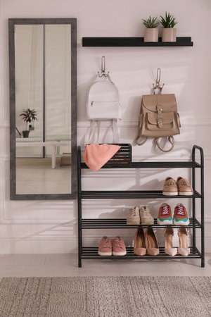 Black shelving unit with shoes and various accessories near white wall in hall. Storage ideasの写真素材