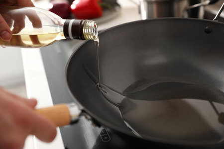 Man pouring cooking oil into frying pan in kitchen, closeupの写真素材
