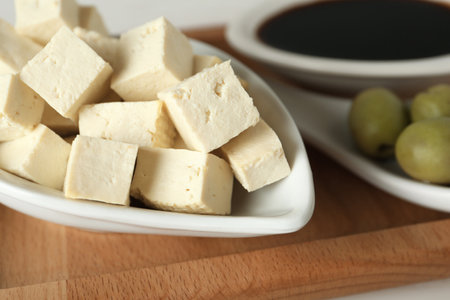 Pieces of delicious tofu and olives on wooden board, closeup. Soybean curdの写真素材