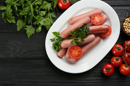 Delicious vegetarian sausages with parsley, tomatoes and soybeans on black wooden table, flat layの写真素材