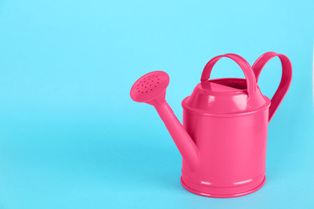 Pink metal watering can on light blue background, space for textの写真素材