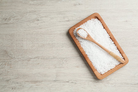Plate and spoon with natural sea salt on light wooden table, top view. Space for textの写真素材