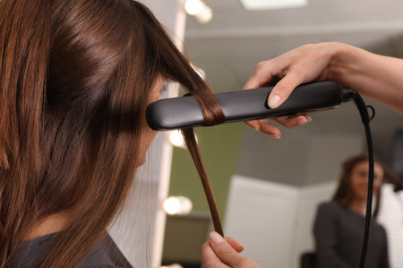 Stylist curling woman's hair with flat iron in salonの写真素材