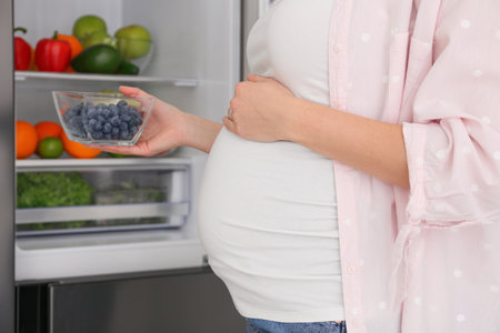 Young pregnant woman with blueberries near fridge at home, closeup. healthy eatingの写真素材