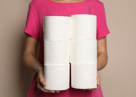 Woman with heap of toilet paper rolls on beige background, closeupの写真素材