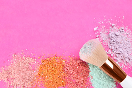 Makeup brush and scattered eye shadows on bright pink background, flat lay. Space for text