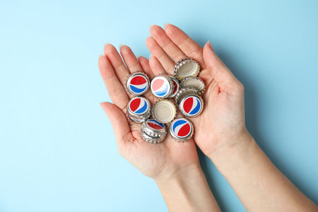 MYKOLAIV, UKRAINE - FEBRUARY 12, 2021: Woman holding Pepsi lids on light blue background, top view