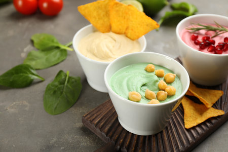 Different kinds of tasty hummus served with nachos on gray table, space for textの写真素材