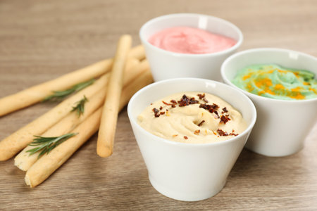 Different kinds of tasty hummus served with bread sticks on wooden tableの写真素材