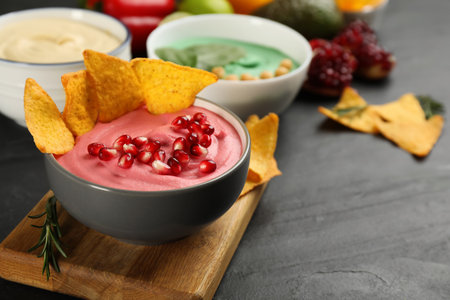 Different kinds of tasty hummus served with nachos on black table, space for text
