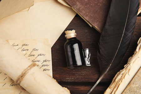 Feather pen, bottle of ink and paper on wooden table, flat lay