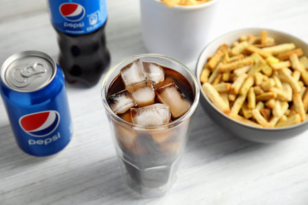MYKOLAIV, UKRAINE - FEBRUARY 15, 2021: Glass of Pepsi, can and snack on white wooden tableのeditorial素材