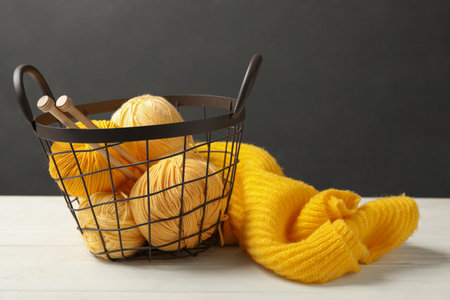Soft yellow woolen yarns with knitting needles and sweater on white tableの写真素材