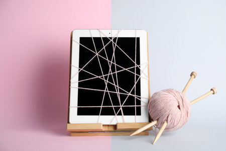 Modern tablet wrapped in thread, yarn ball and knitting needles on color background. internet addiction conceptの写真素材