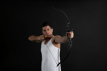 Man with bow and arrow practicing archery on black backgroundの写真素材